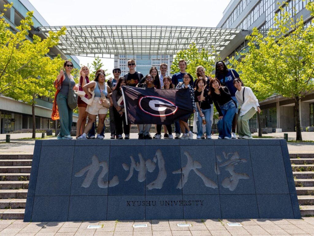 Several students hold a UGA "G" flag at Kyushu University in Japan.