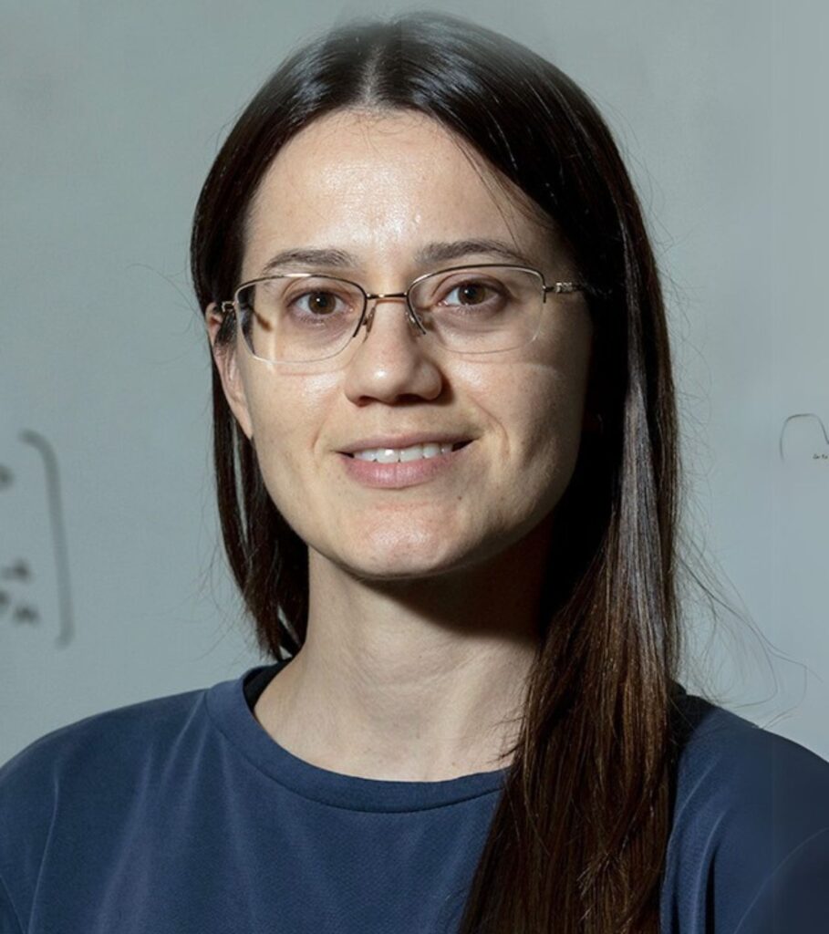 An individual smiling at the camera against a whiteboard in the background.