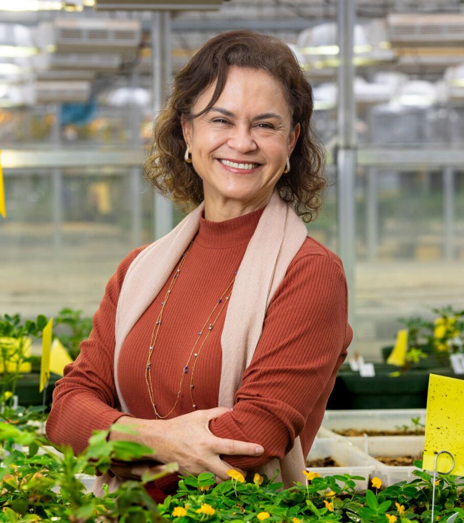 An individual in a greenhouse setting smiling at the camera.