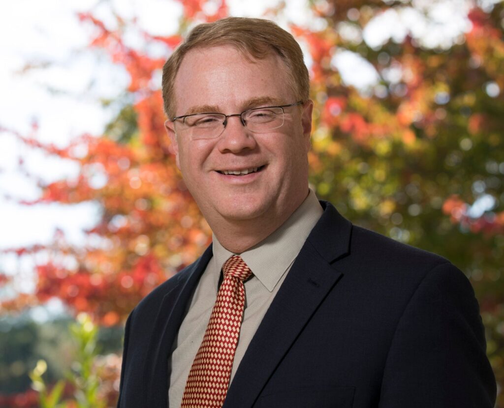 An individual wearing a suit in an outdoor setting smiling at the camera.