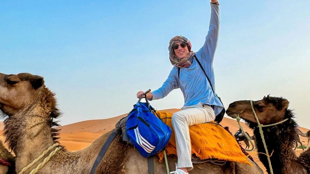 Male student riding camel in desert.